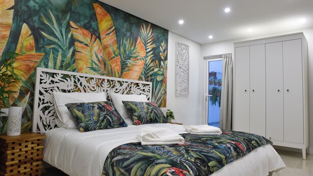 Een slaapkamer met een bed, een groot tropisch muurschildering, een wit hoofdeinde en een kledingkast.