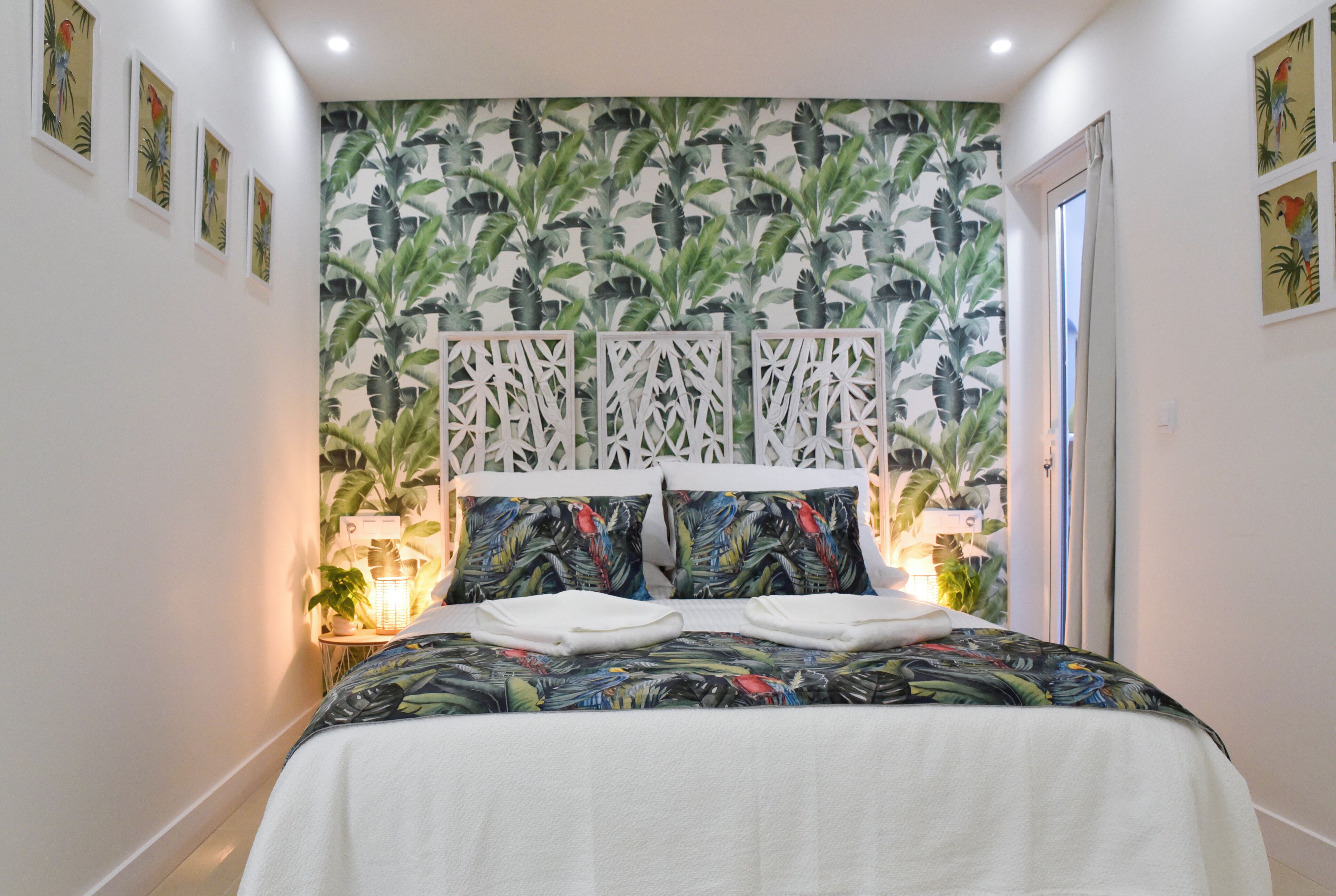 Un dormitorio con una cama, un cabecero decorativo y una pared con un estampado de hojas tropicales.