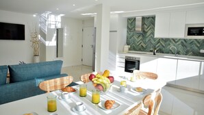 Een moderne keuken met witte kasten, een mozaïek achterwand in een visgraatpatroon en een flatscreen televisie aan de muur.