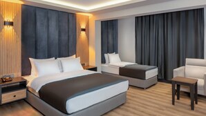 A modern hotel room with a large bed, a sofa, a chair, and a small table. There are two nightstands with lamps and a phone. - Yeşilton Otel (Arhavi)