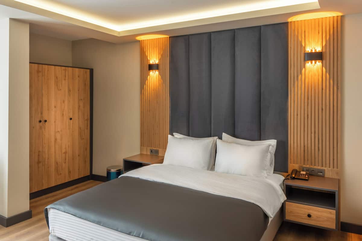 A modern hotel room with a large bed, wooden wardrobe, and built-in wall sconces.