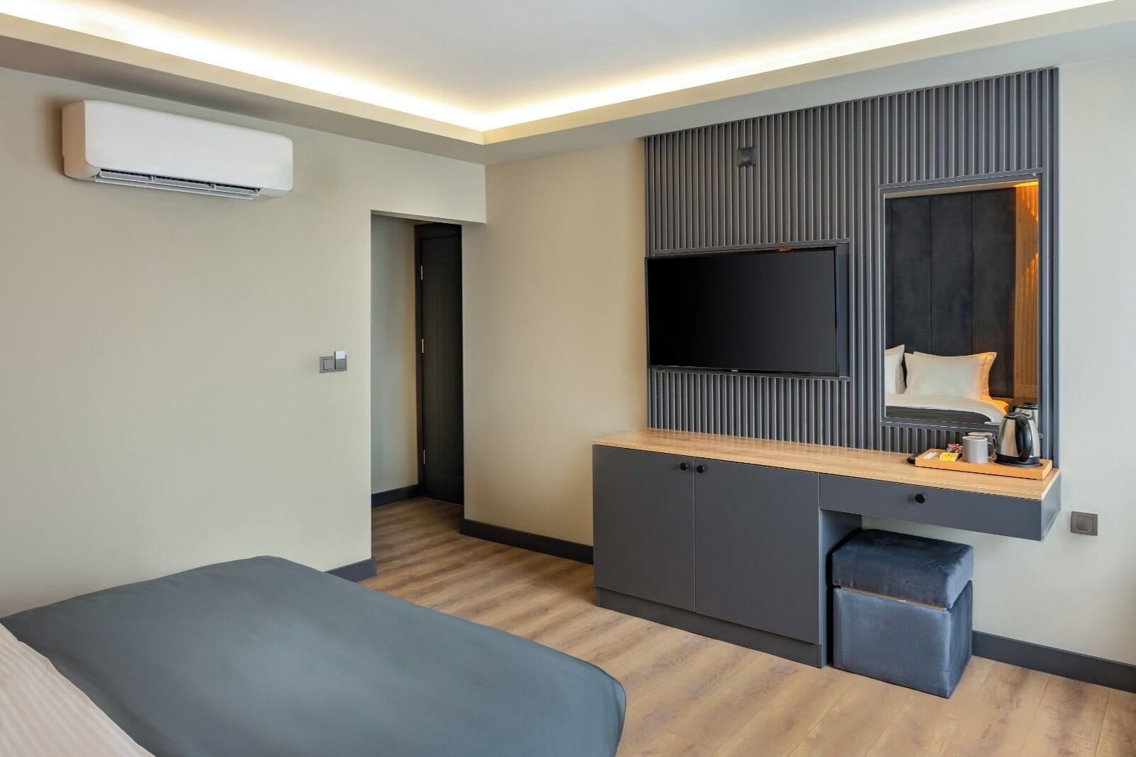 Una habitación de hotel moderna con un televisor de pantalla plana montado en la pared, un escritorio de madera con un espejo y una pequeña zona de estar.