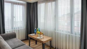 A modern living room with a grey sofa, a wooden dining table with a fruit bowl, and a glass of wine. - Yeşilton Otel (Arhavi)