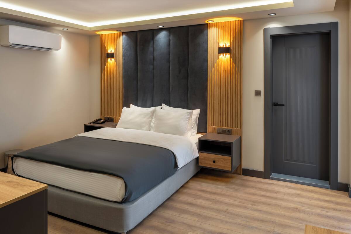 A modern bedroom with a large bed, bedside tables, an air conditioning unit, and a door.
