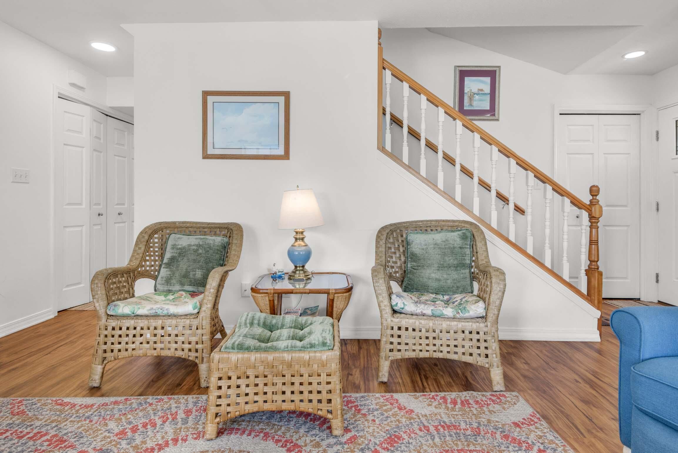 A living room with wicker furniture, a wooden staircase, and a patterned rug.