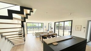 Una cocina moderna con una isla central, una zona de comedor con una mesa y sillas, y una escalera de diseño minimalista.
