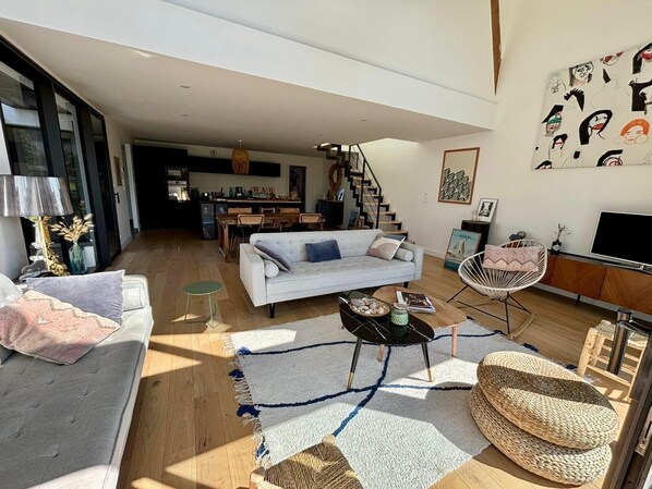 A modern living room with a sofa, coffee table, and a TV. There is a staircase leading to a kitchen area.