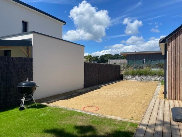 A modern outdoor area with a barbecue grill, a wooden deck, and a gravel space.