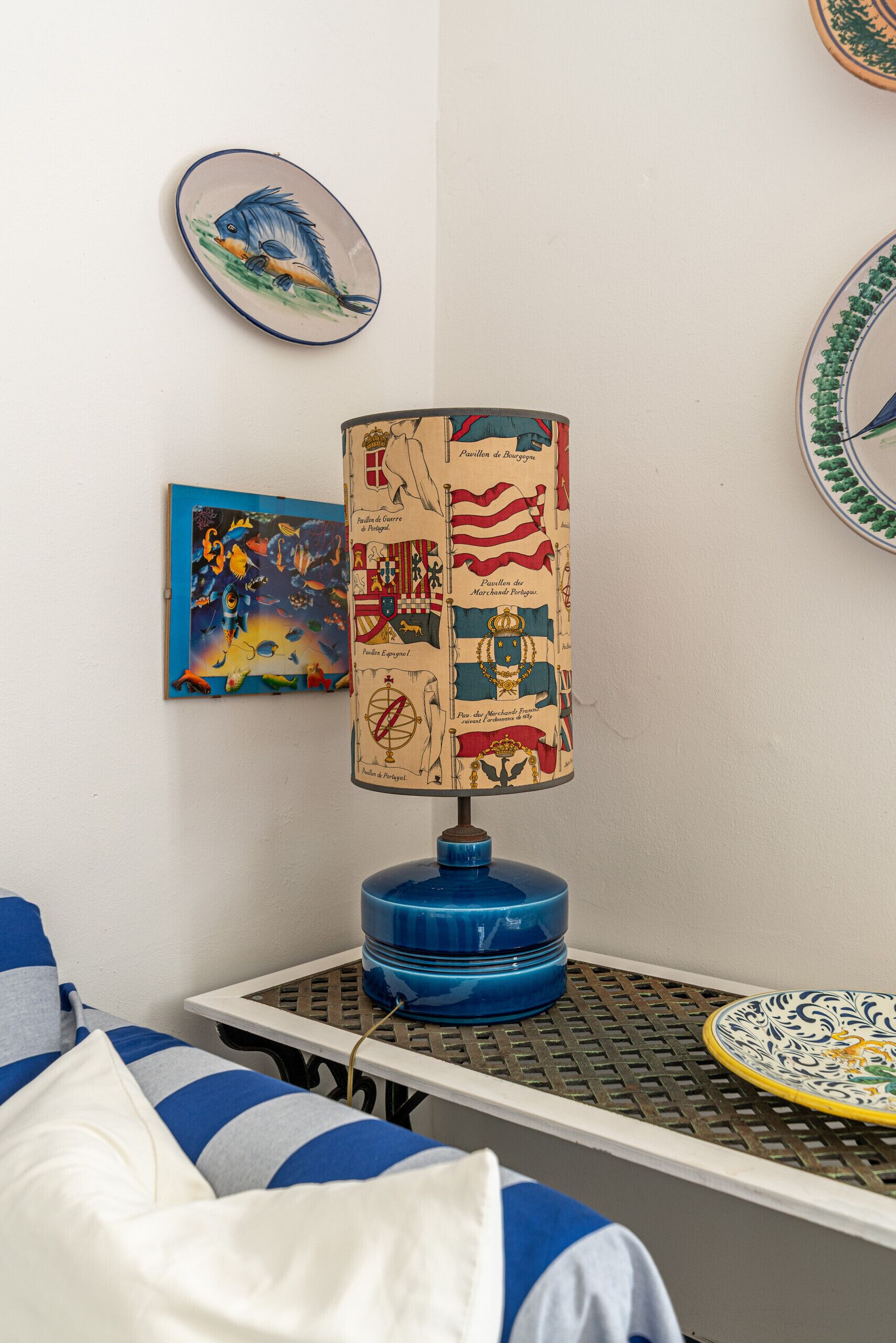 A room with a bed, a table with a lamp, and decorative plates on the wall.