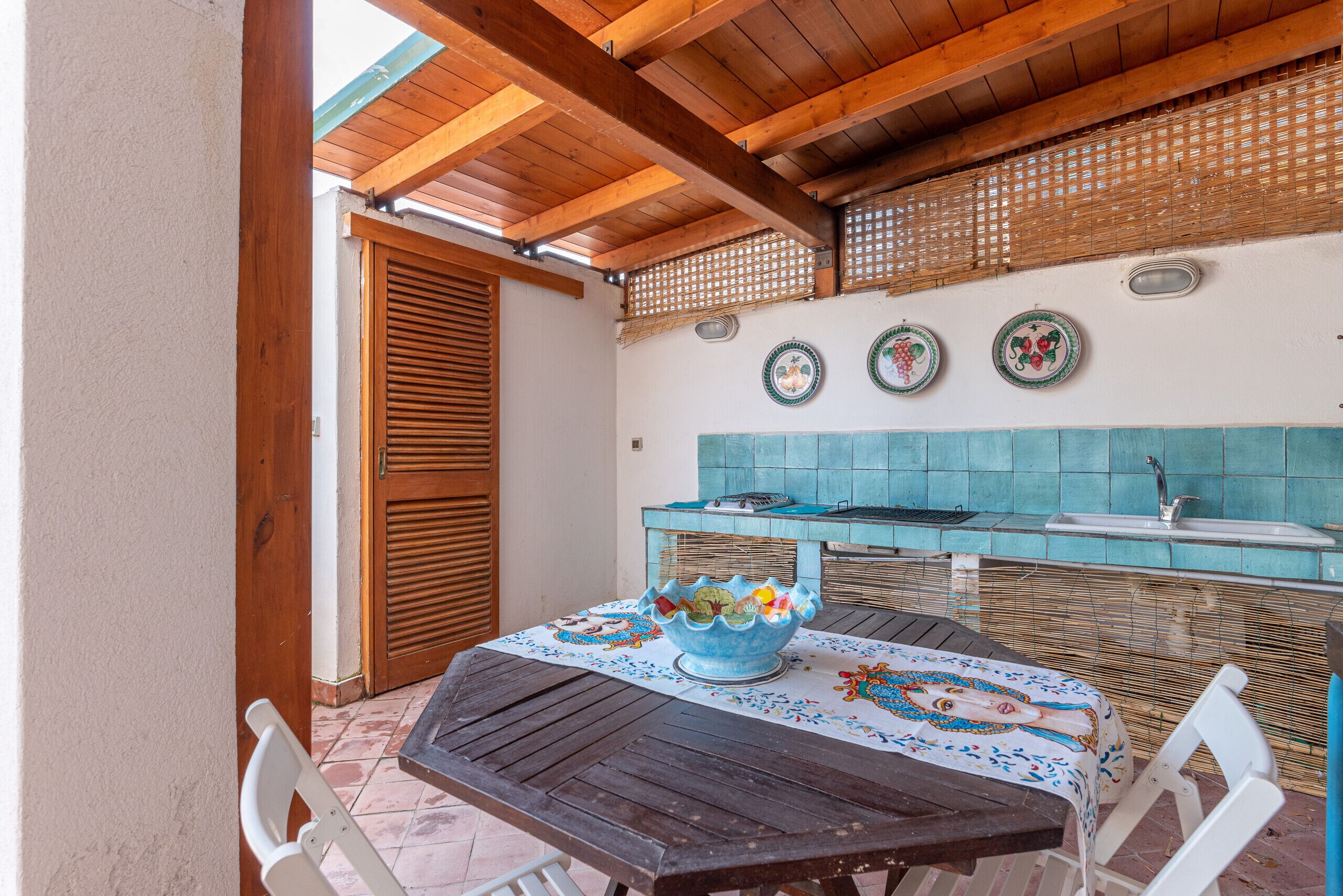 An outdoor kitchen area with a wooden table, chairs, and a decorative bowl.