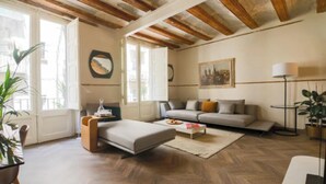 A living room with a sofa, ottoman, coffee table, and a lamp. - Historic Charm Meets Modern Comfort (Barcelona)