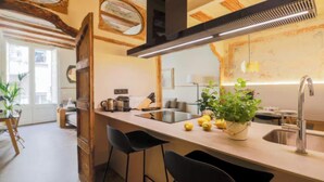 A modern kitchen with a central island, bar stools, a sink, and a potted plant. - Historic Charm Meets Modern Comfort (Barcelona)
