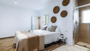 A bedroom with a bed, a bedside table, a mirror, and a shower area. - Historic Charm Meets Modern Comfort (Barcelona)