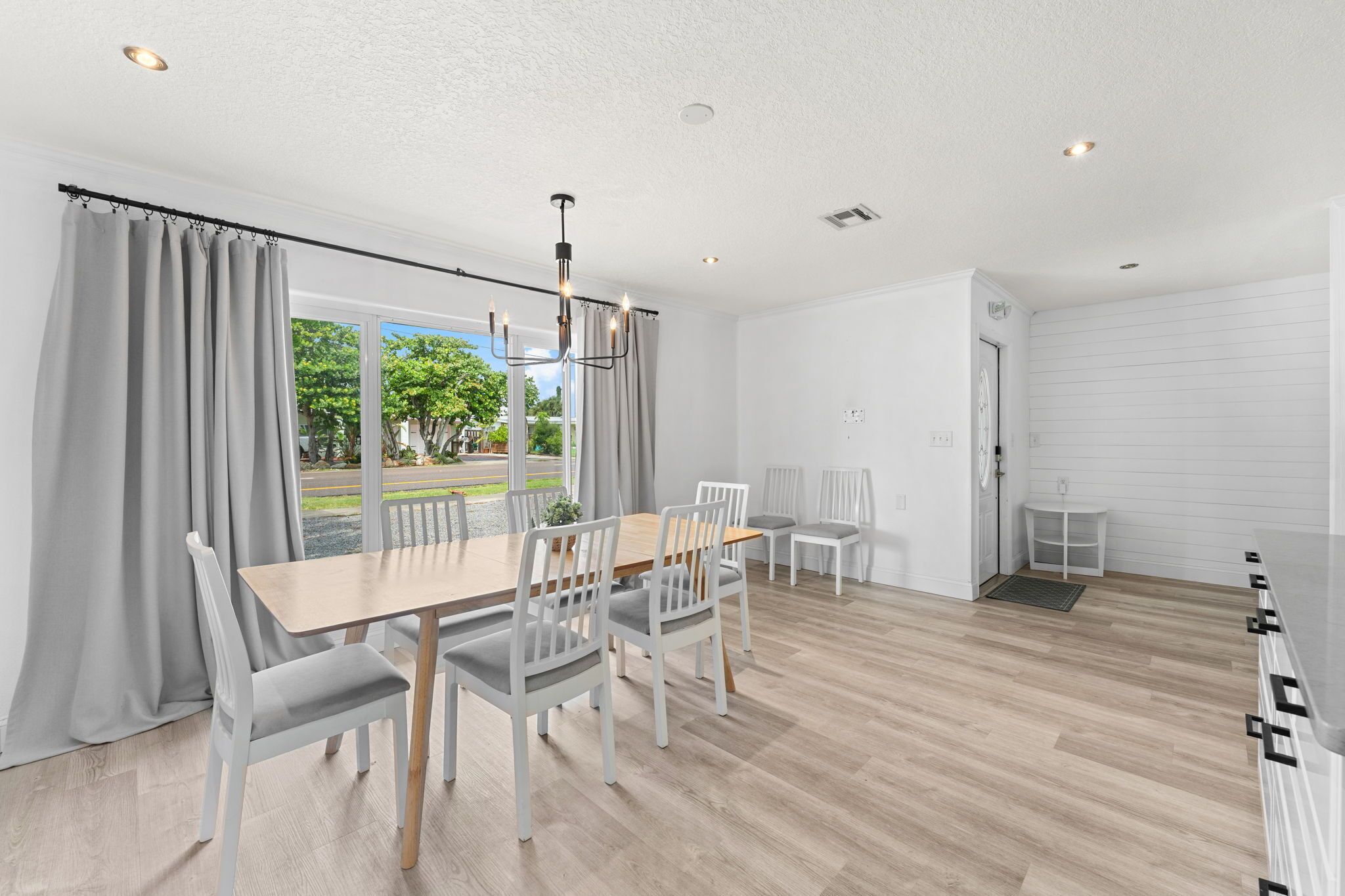 Un comedor moderno con una mesa de madera y sillas blancas, un candelabro y vistas al exterior con vegetación.