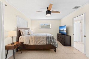 A bedroom with a bed, a TV, a ceiling fan, a window, and a door.