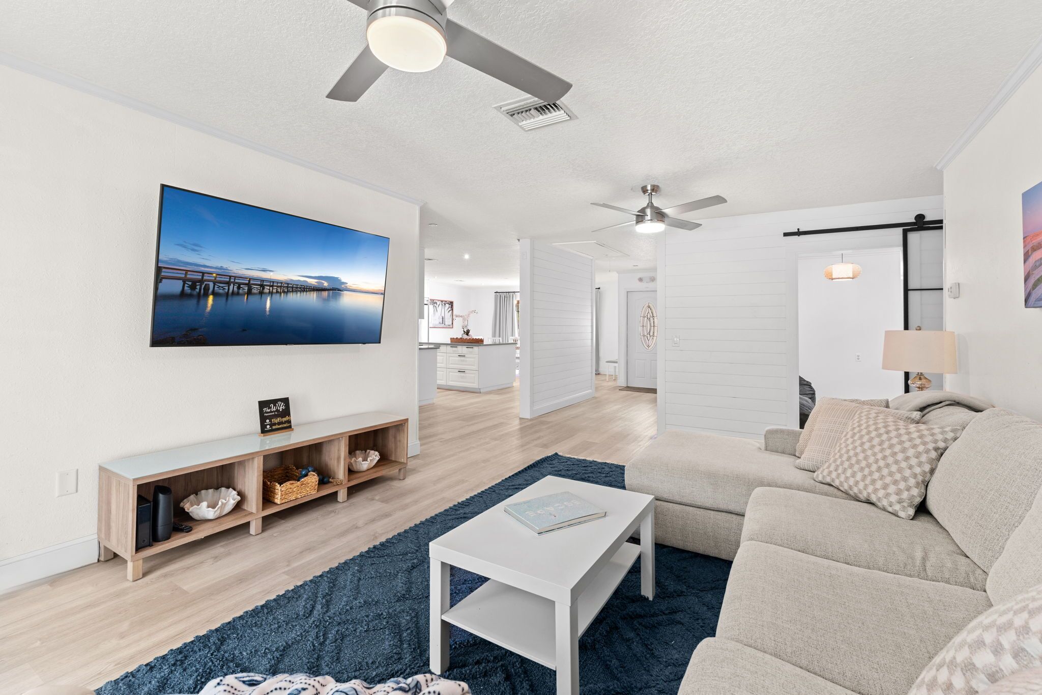 A modern living room with a large flat-screen TV, a sofa, a coffee table, and a wooden console table with decorative items.