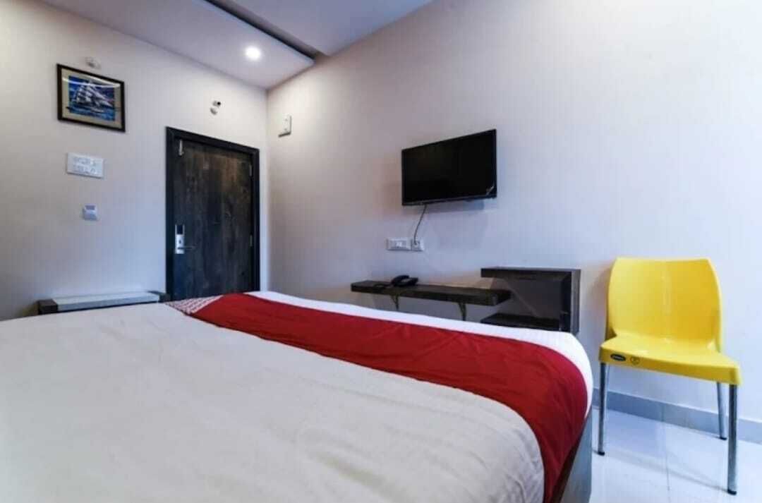 Une chambre d’hôtel avec un lit, un téléviseur fixé au mur, un bureau et une chaise jaune.