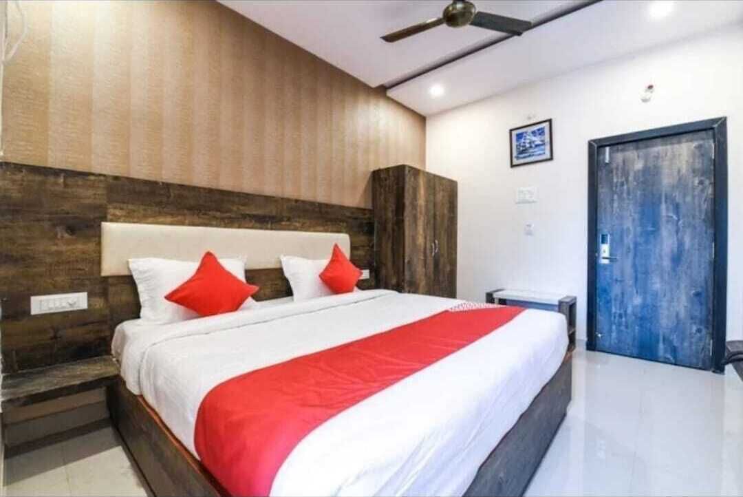 Quarto de hotel com cama, cabeceira de madeira, colcha vermelha e branca, ventilador de teto e porta azul.