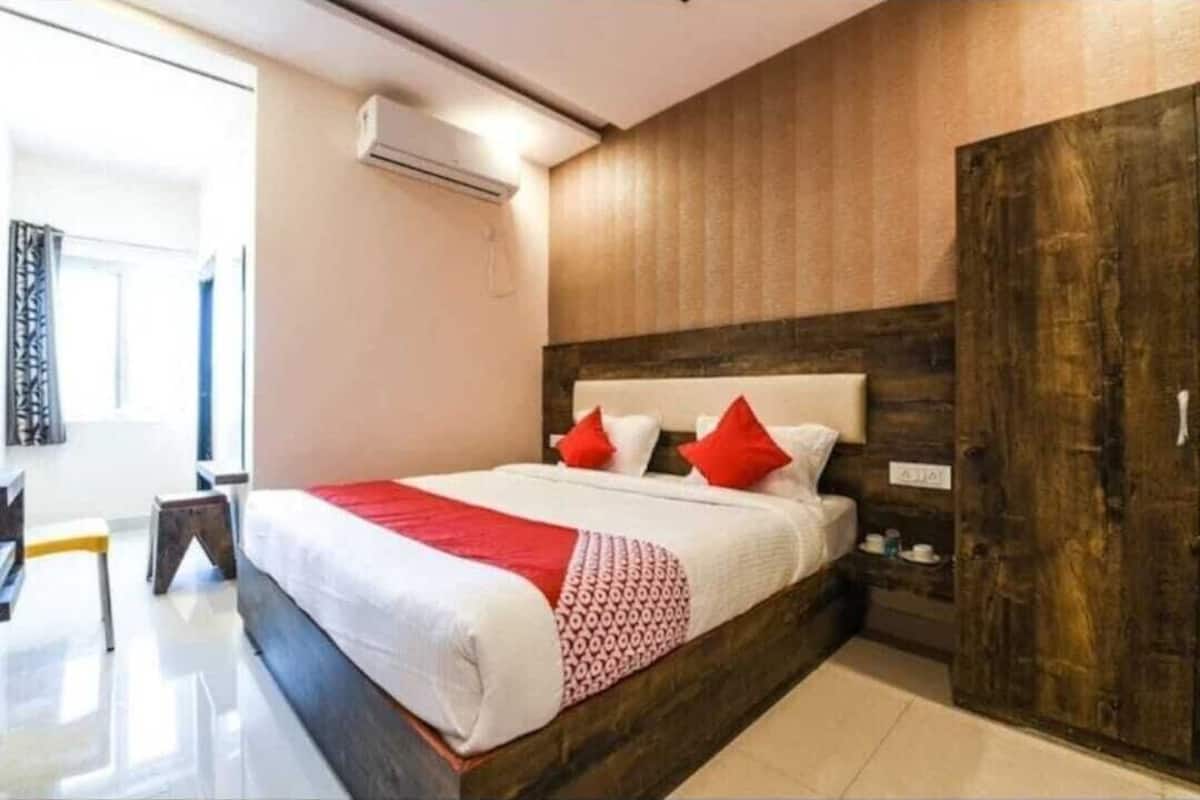 A modern hotel room with a large bed, a wooden headboard, and a wardrobe.