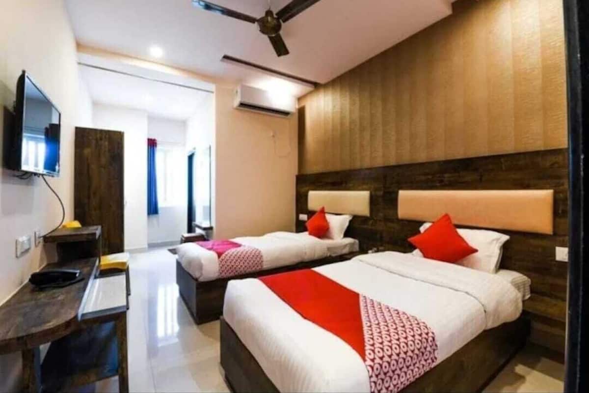 A hotel room with two beds, a desk, a television, and a ceiling fan.