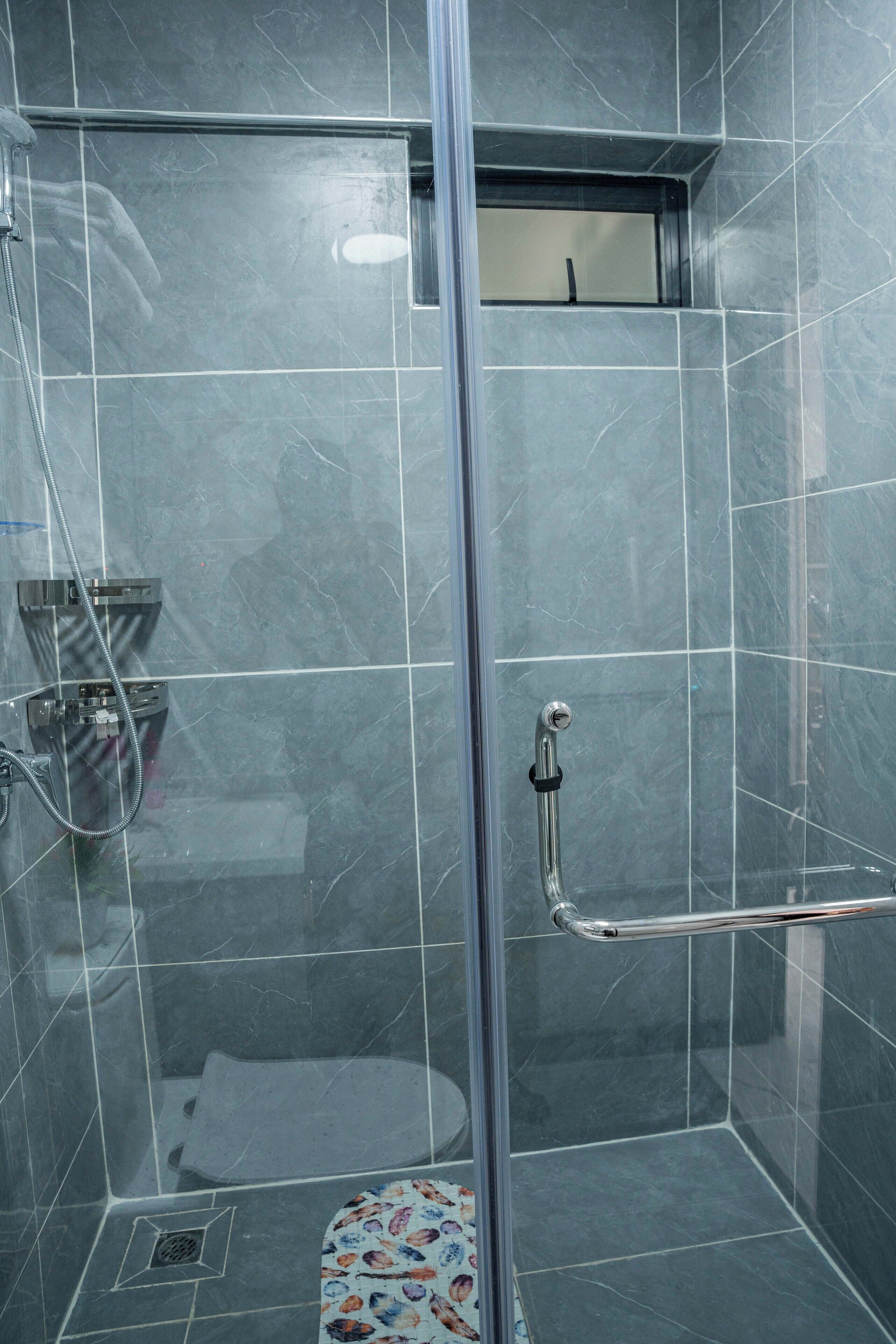 A glass-enclosed shower stall with a handrail, a showerhead, and a small window.