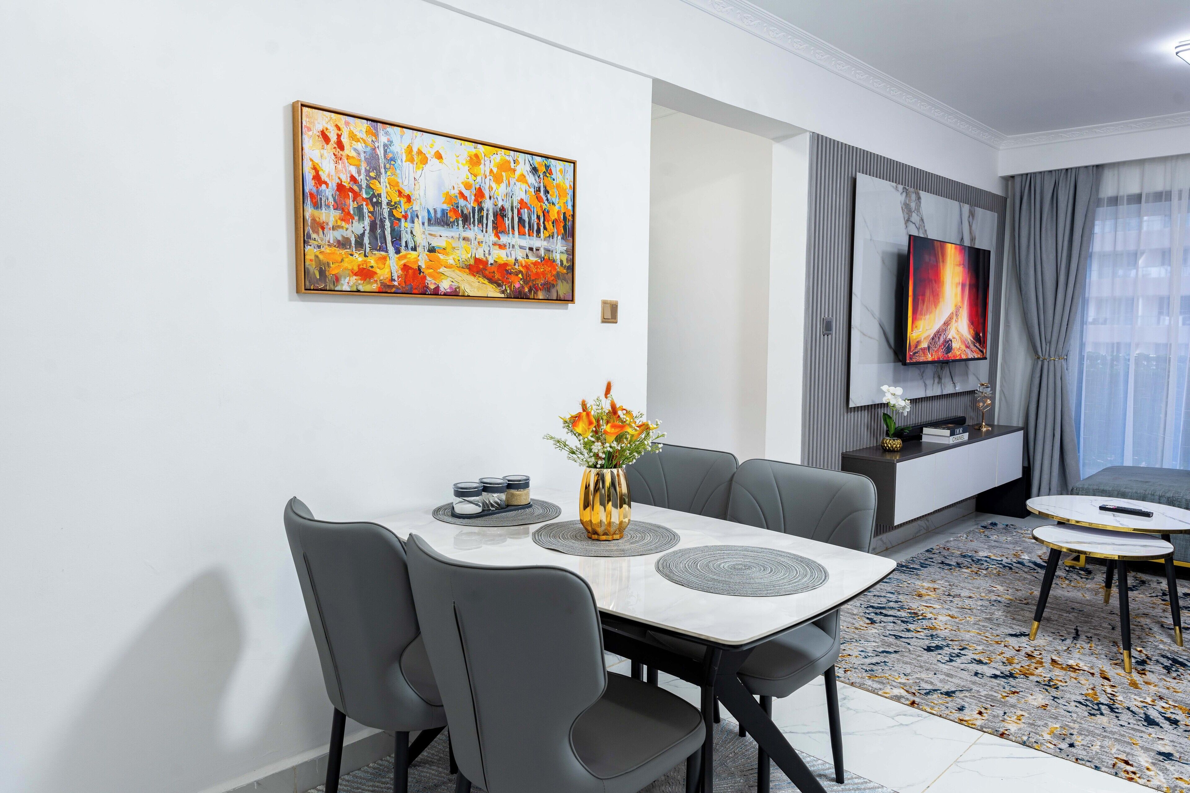 A modern living room with a dining area, a flat-screen TV, and a painting on the wall.