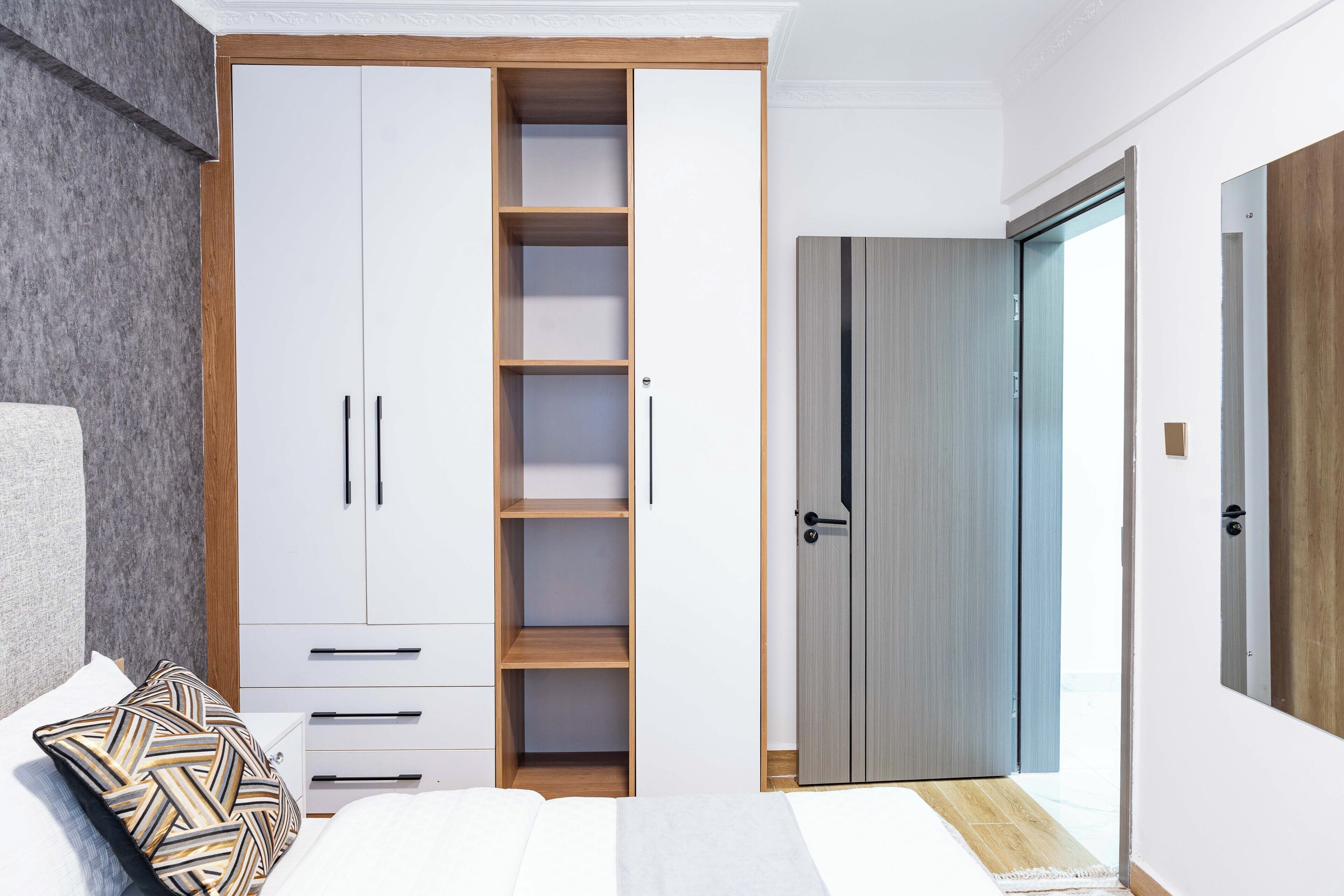 A bedroom with a bed, a wardrobe with multiple compartments, and a door leading to another room.