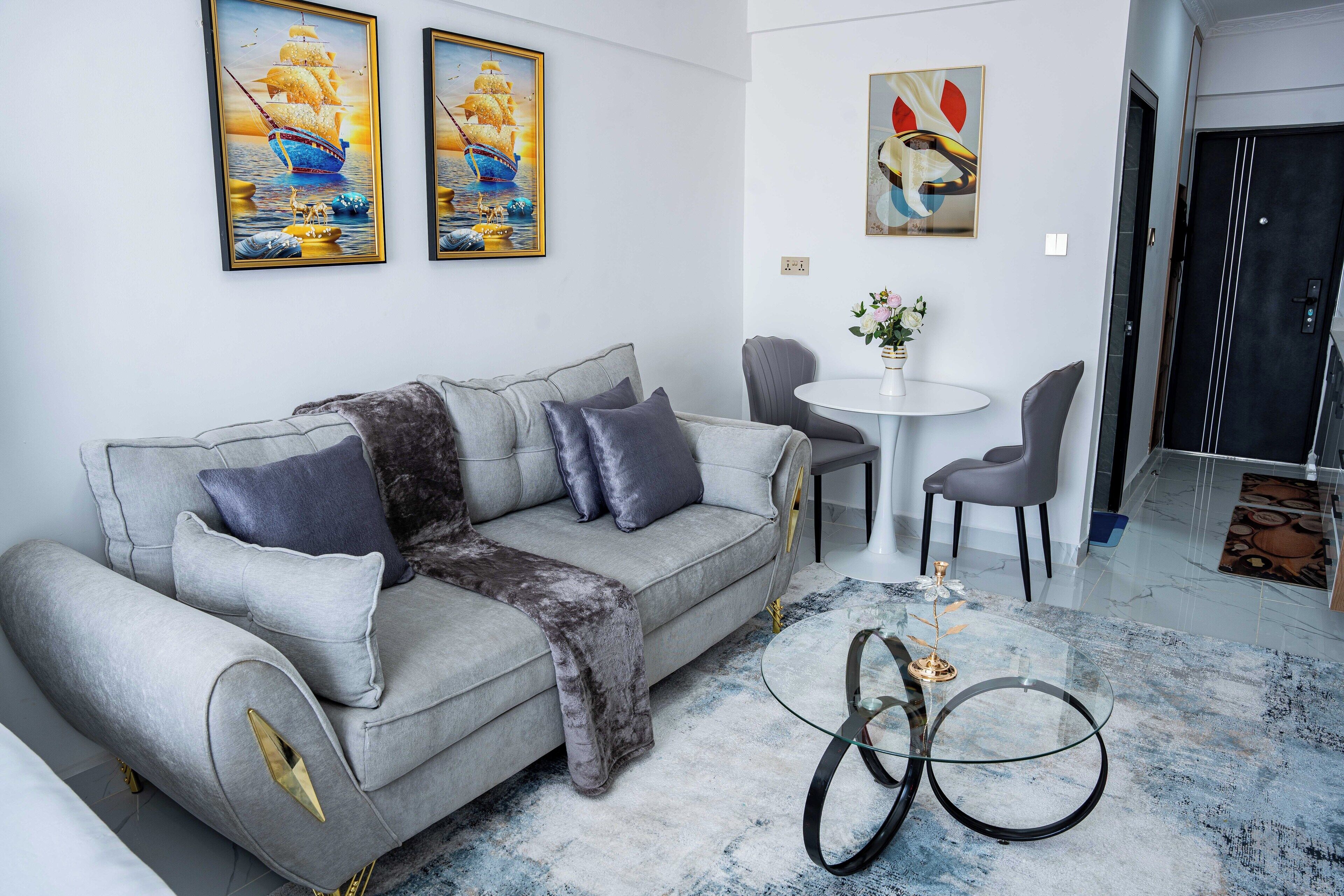 A modern living room with a grey sofa, a round coffee table, and a painting of a ship on the wall.