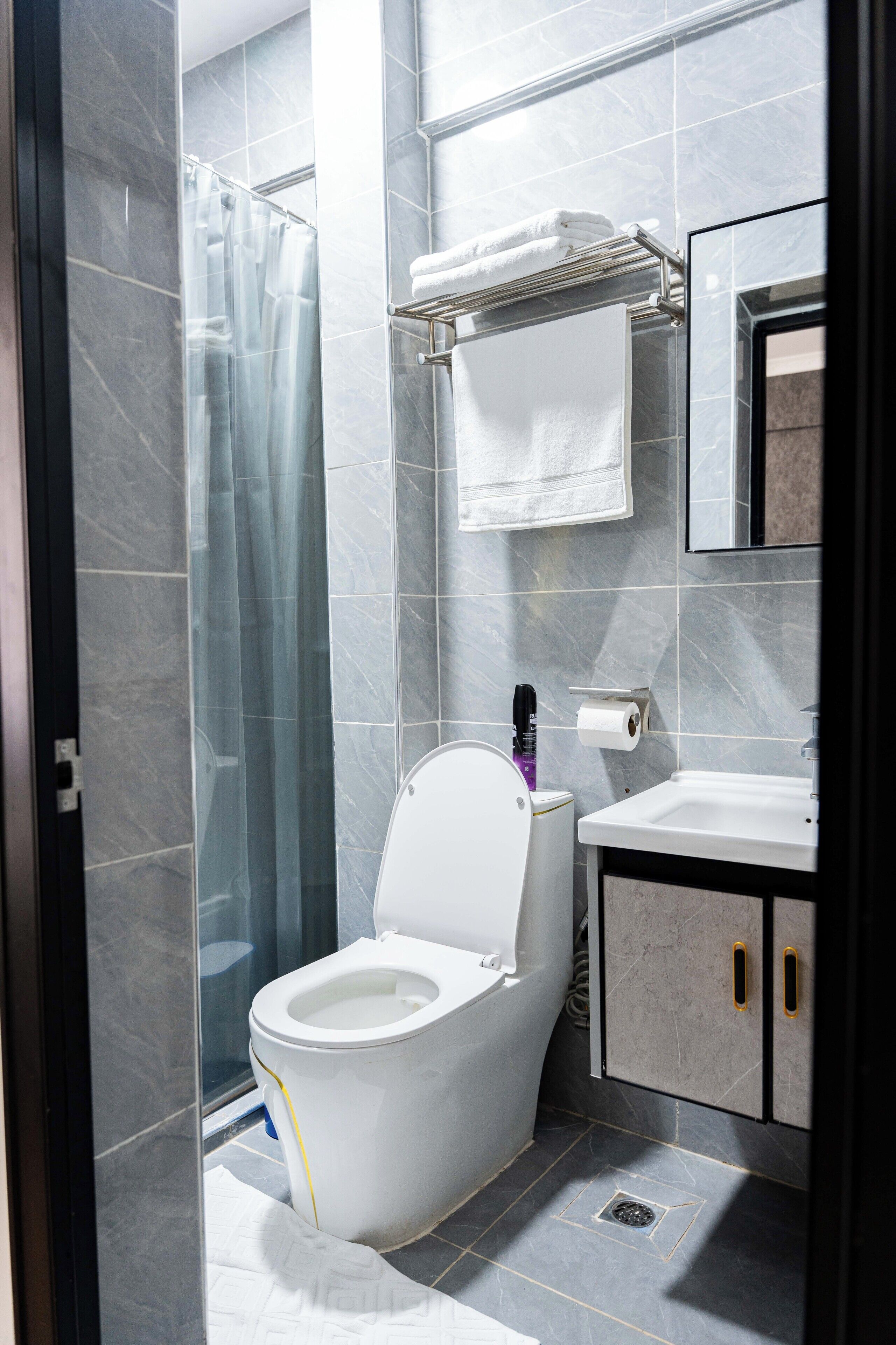 A modern bathroom with a glass shower enclosure, a white toilet, a sink, and a towel rack.