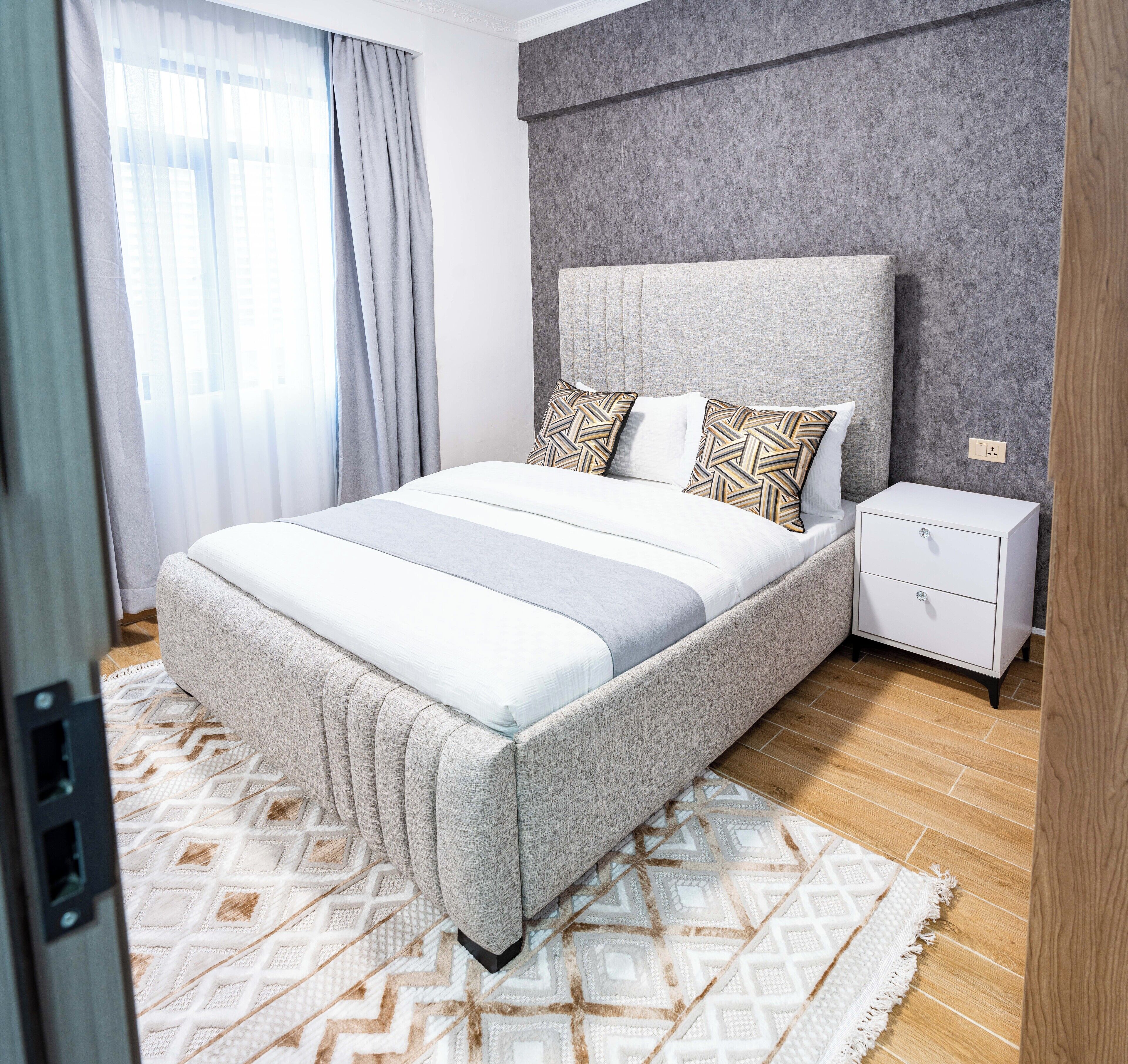 A bedroom with a bed, a nightstand, a power outlet, and a patterned rug.