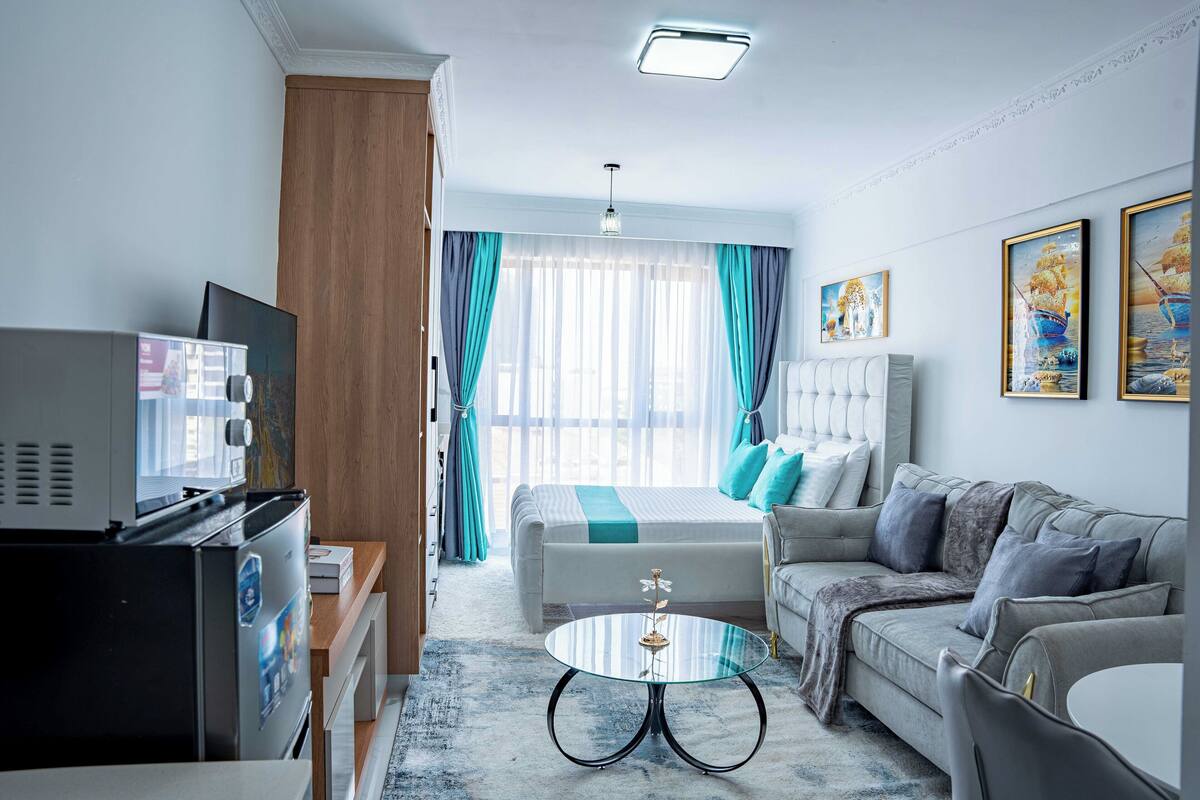 A modern hotel room with a bed, sofa, TV, and a small table.