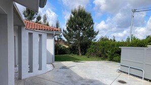 A concrete patio area with a tiled roof structure, a metal fence, and a large tree in the background. - 4-bedroom villa, private heated pool, enclosed garden8 minutes from the beach (Linxe)
