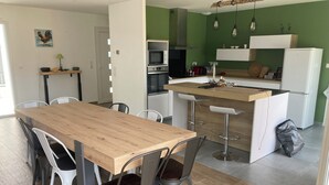 A modern kitchen with a wooden island, white cabinets, and a green accent wall. - 4-bedroom villa, private heated pool, enclosed garden8 minutes from the beach (Linxe)