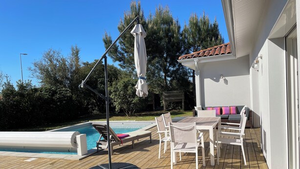 A wooden deck with a pool, lounge chairs, and a table with chairs. - 4-bedroom villa, private heated pool, enclosed garden8 minutes from the beach (Linxe)