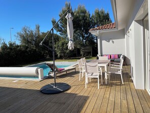 Una terraza de madera con piscina, sillas de descanso y una mesa con sillas.