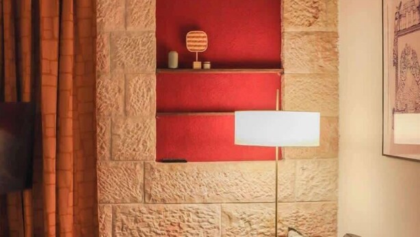 Un salon avec un mur en pierre, une étagère rouge, un canapé en cuir noir et une table basse en bois.