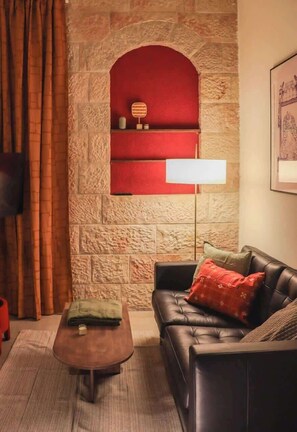 Una sala de estar con una pared de piedra, un estante rojo, un sofá de cuero negro y una mesa de centro de madera.