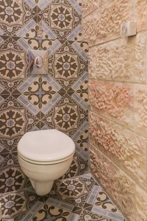 Un baño con baldosas estampadas, un inodoro y un dispensador de jabón en la pared.