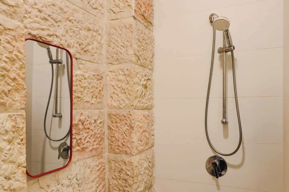 A bathroom with a stone wall and two shower fixtures, one with a mirror.