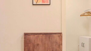 Une pièce avec un meuble en bois adossé au mur, un tableau abstrait encadré au-dessus, et un meuble blanc sur la droite.