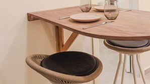 Un coin repas avec une table en bois, deux chaises en osier et un tableau abstrait encadré accroché au mur.