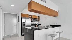 A modern kitchen with a central island, stainless steel appliances, and wooden cabinetry. - Edgewater High-Rise | Stunning Bay Views + Gym (Miami)