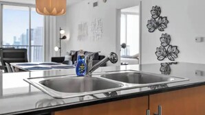 A modern kitchen with a double sink, a hanging pendant light, and a bottle of dish soap on the counter. - Edgewater High-Rise | Stunning Bay Views + Gym (Miami)