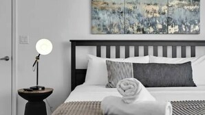 A neatly made bed with a striped blanket, a bedside lamp, and a painting above the bed. - Edgewater High-Rise | Stunning Bay Views + Gym (Miami)