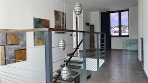 A modern staircase with glass railings and metal accents, leading to a room with large windows and artwork on the walls.