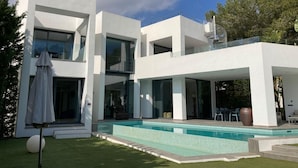 A modern two-story house with a swimming pool, large windows, and a balcony.