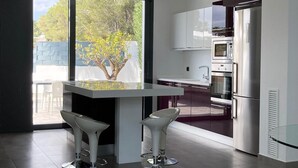 A modern kitchen with a large window, white cabinetry, stainless steel appliances, and two bar stools.