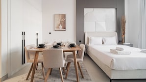 A modern hotel room with a bed, bedside table, and a dining area with a table and chairs. - Quiet Top-Floor Studio Near Metro + Baby Gear (Dubai)