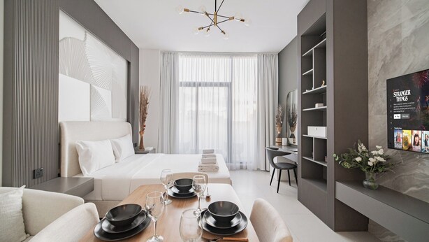 A modern hotel room with a neatly arranged dining area, a large bed, and a television displaying 'Stranger Things'. - Quiet Top-Floor Studio Near Metro + Baby Gear (Dubai)