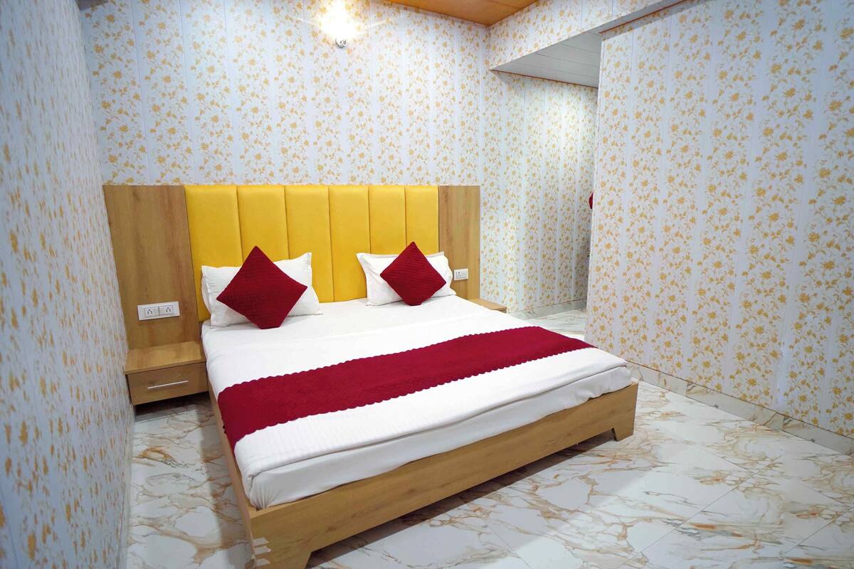 A bedroom with a wooden bed frame, a yellow headboard, and floral wallpaper.